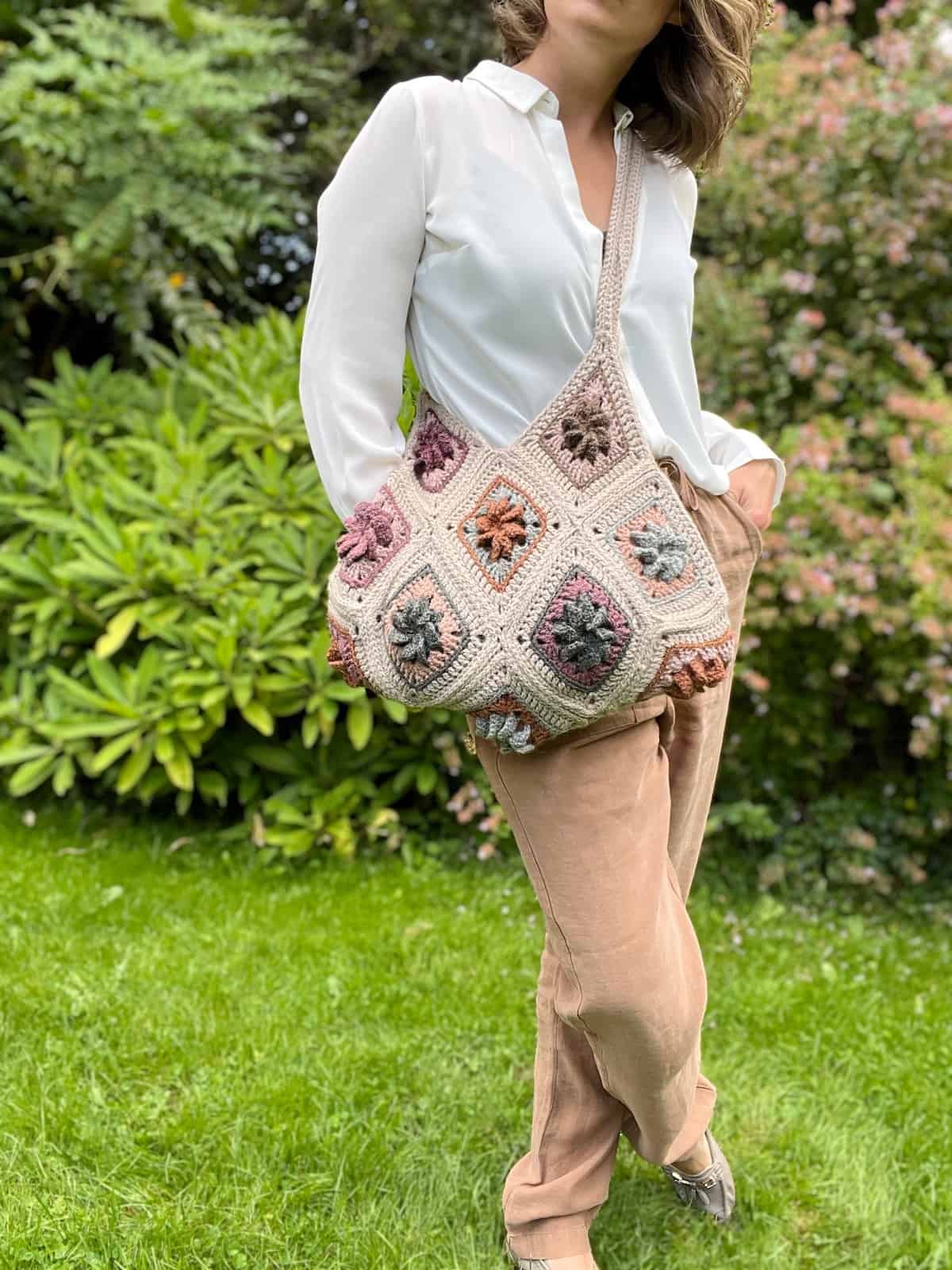 A woman holding a crocheted bag in the grass.