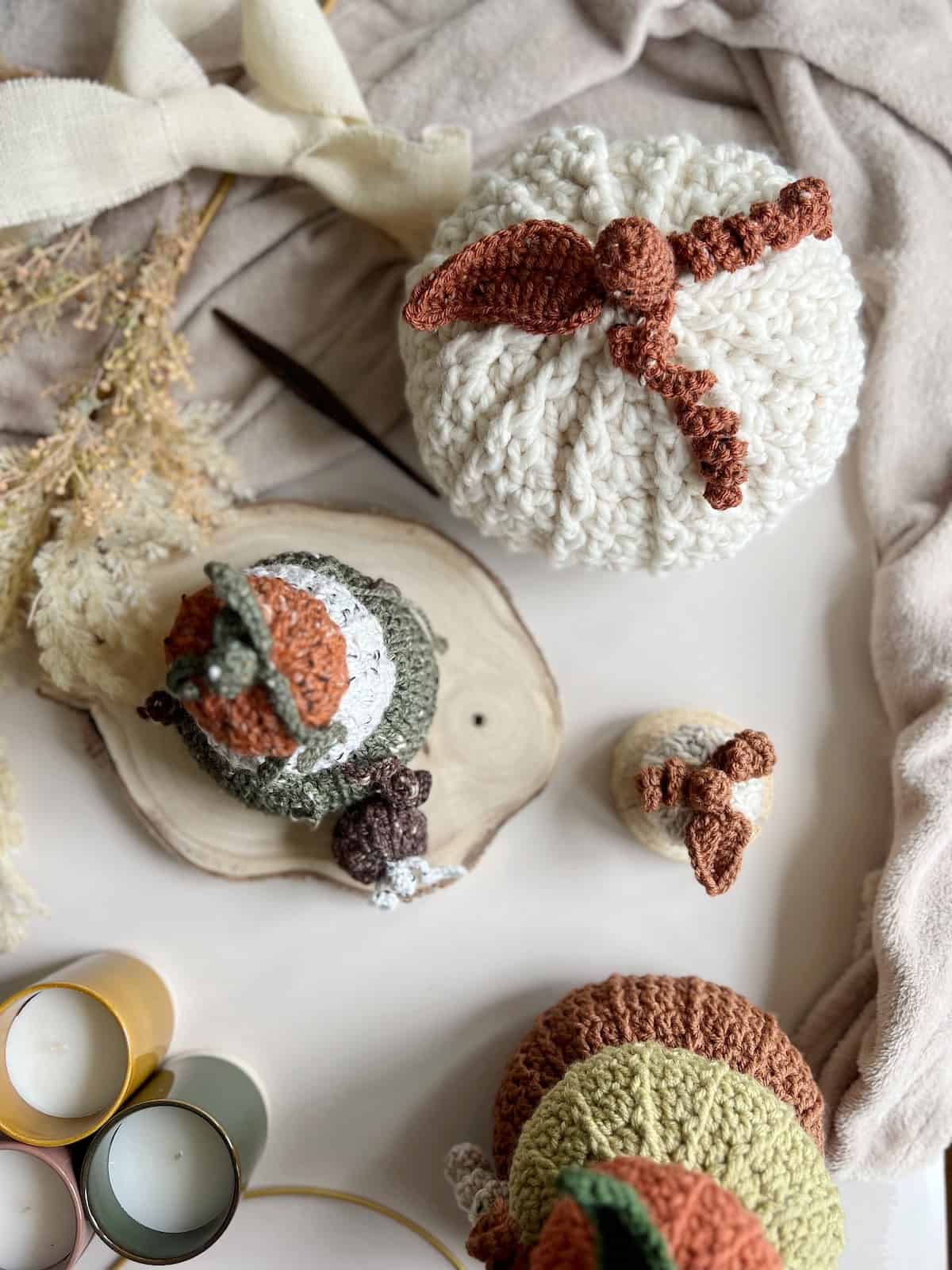 Crocheted pumpkins, candles and crochet hooks on a table.