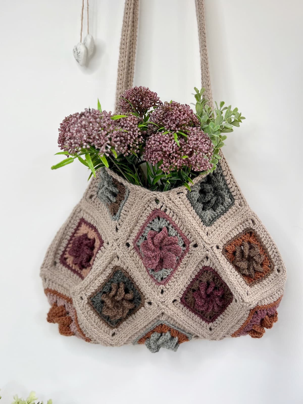 A crocheted bag with flowers hanging from it.
