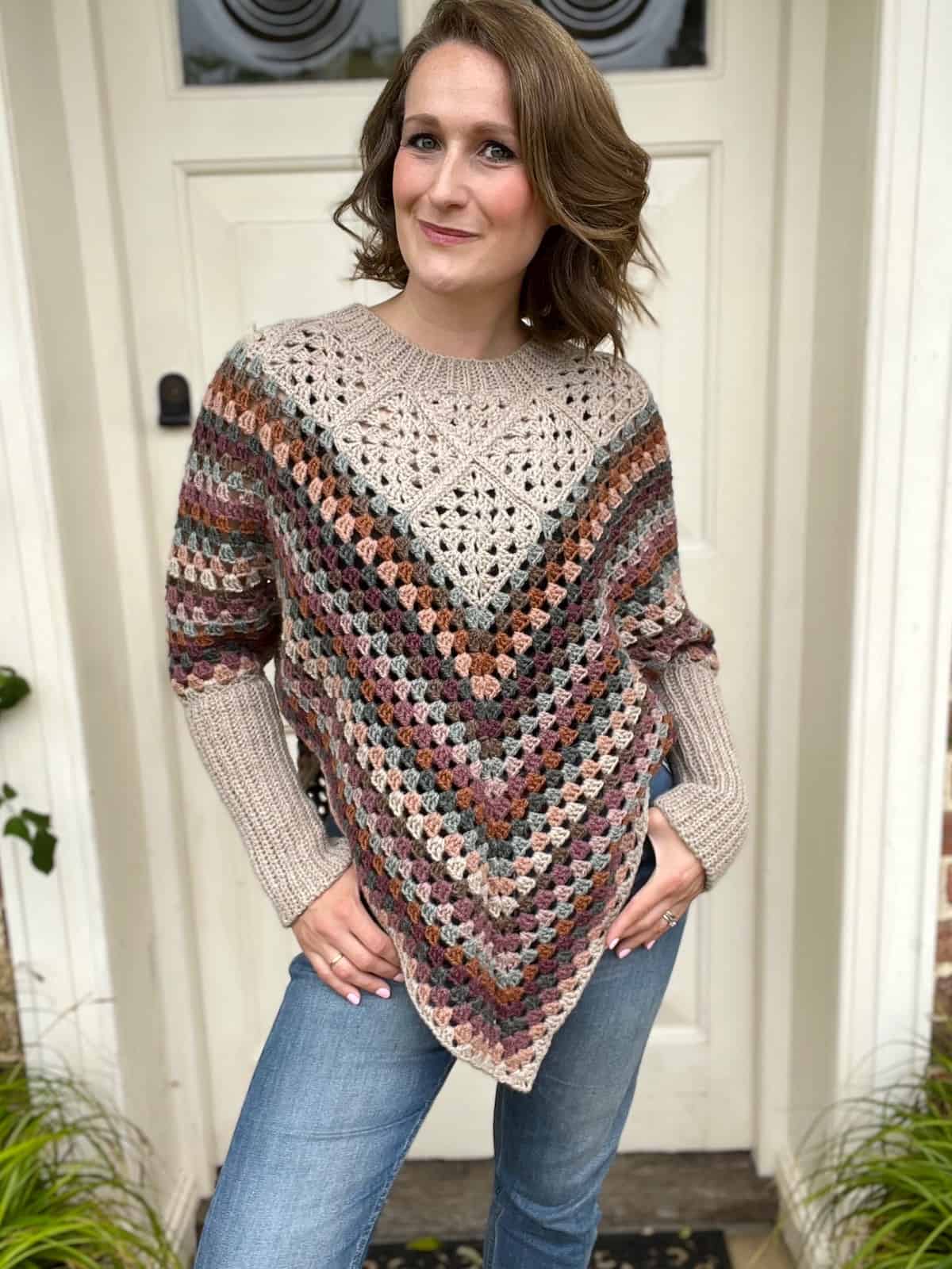 A woman wearing a crocheted granny square poncho standing in front of a door.