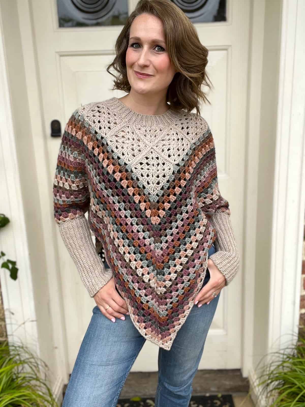 A woman wearing a crocheted poncho standing in front of a door.