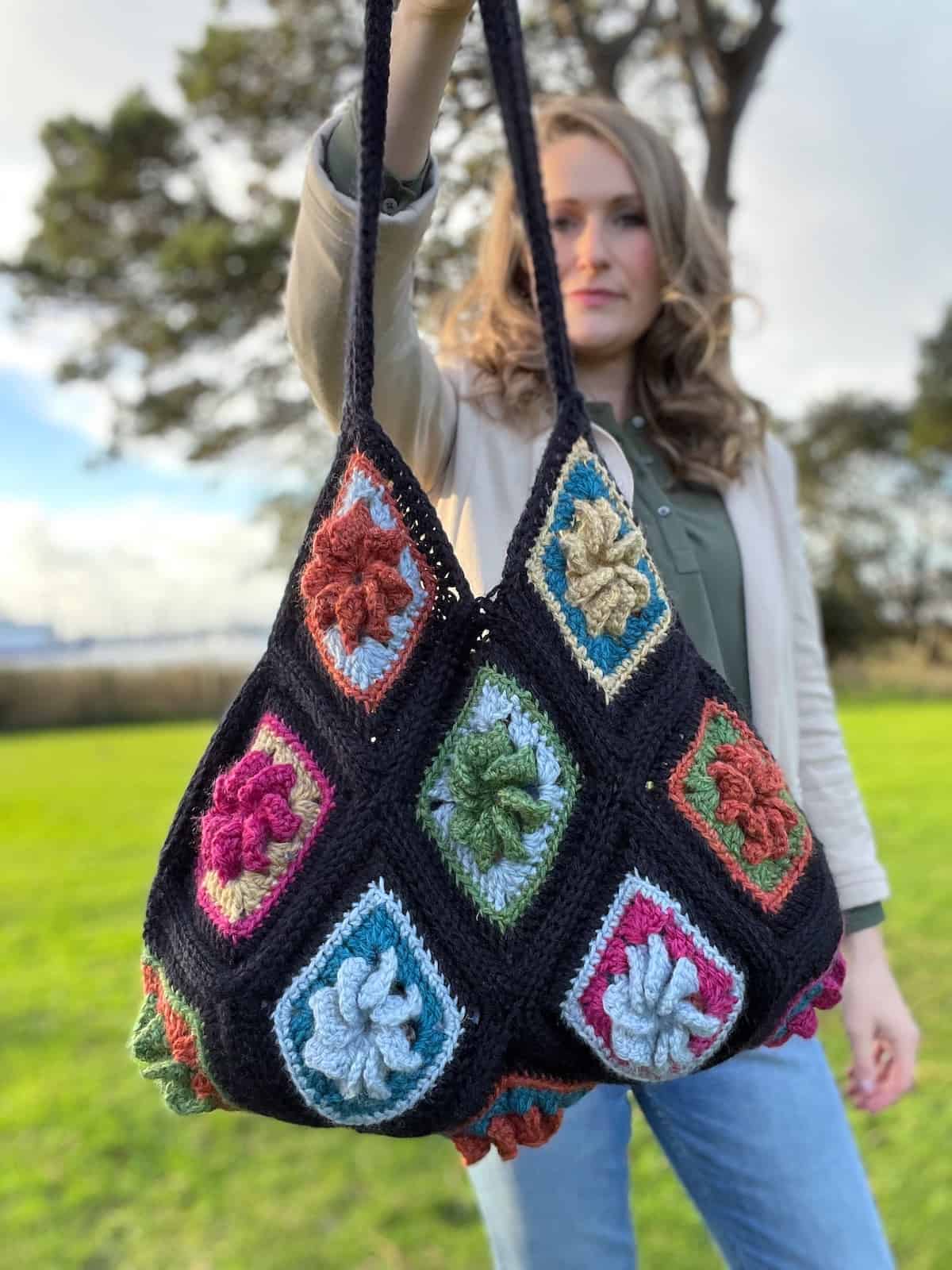 A woman holding a crocheted bag in the grass.