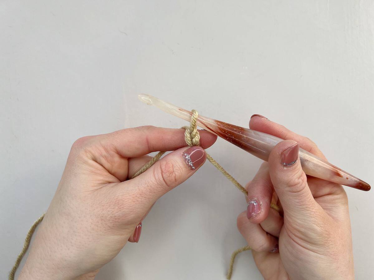 A person is holding a crocheted chain. They have completed the steps to make a chain stitch and will now continue making a foundation chain.