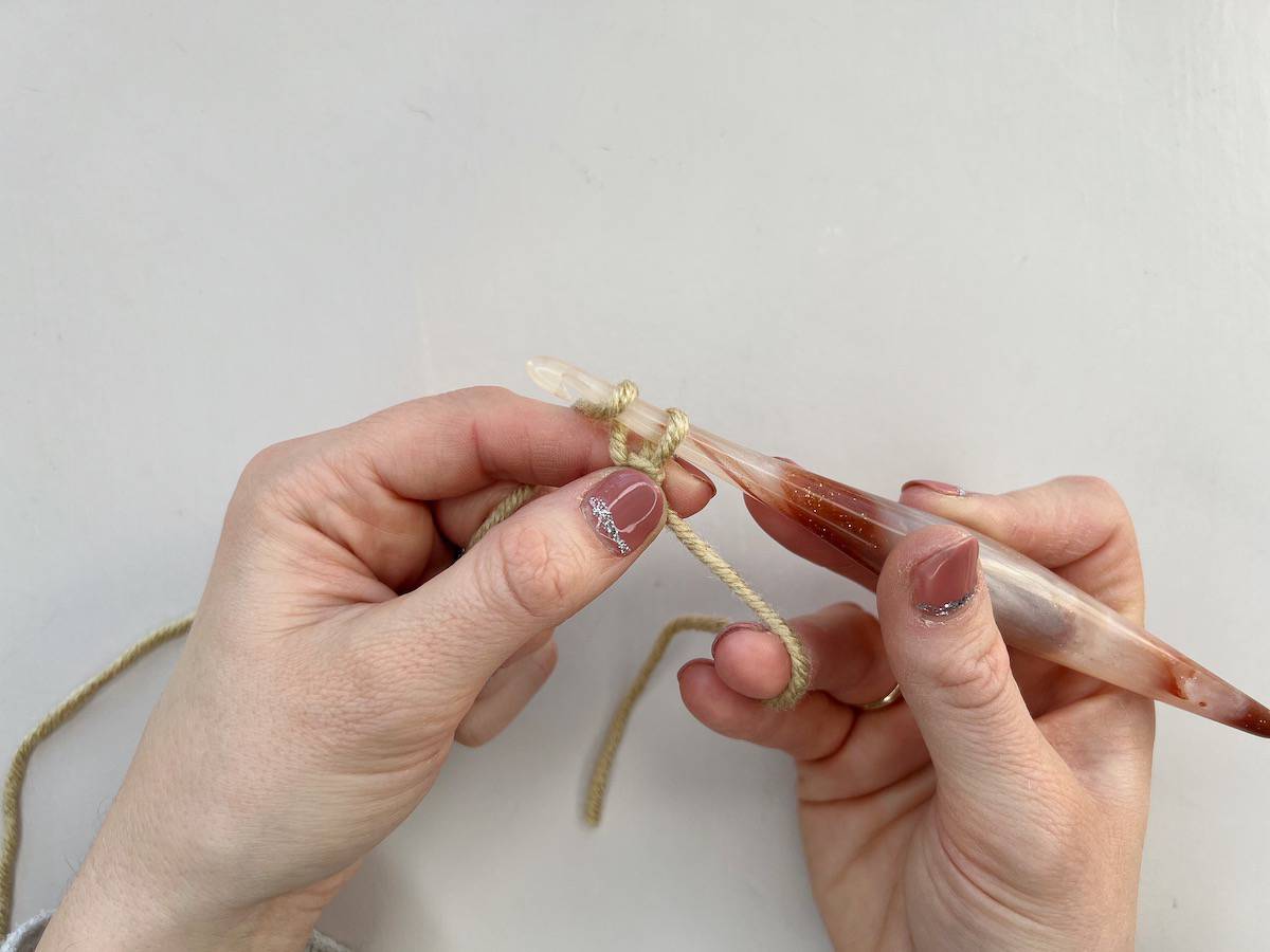 To complete the final step of a chain stitch, a person is drawing the loop through the slipknot previously created.