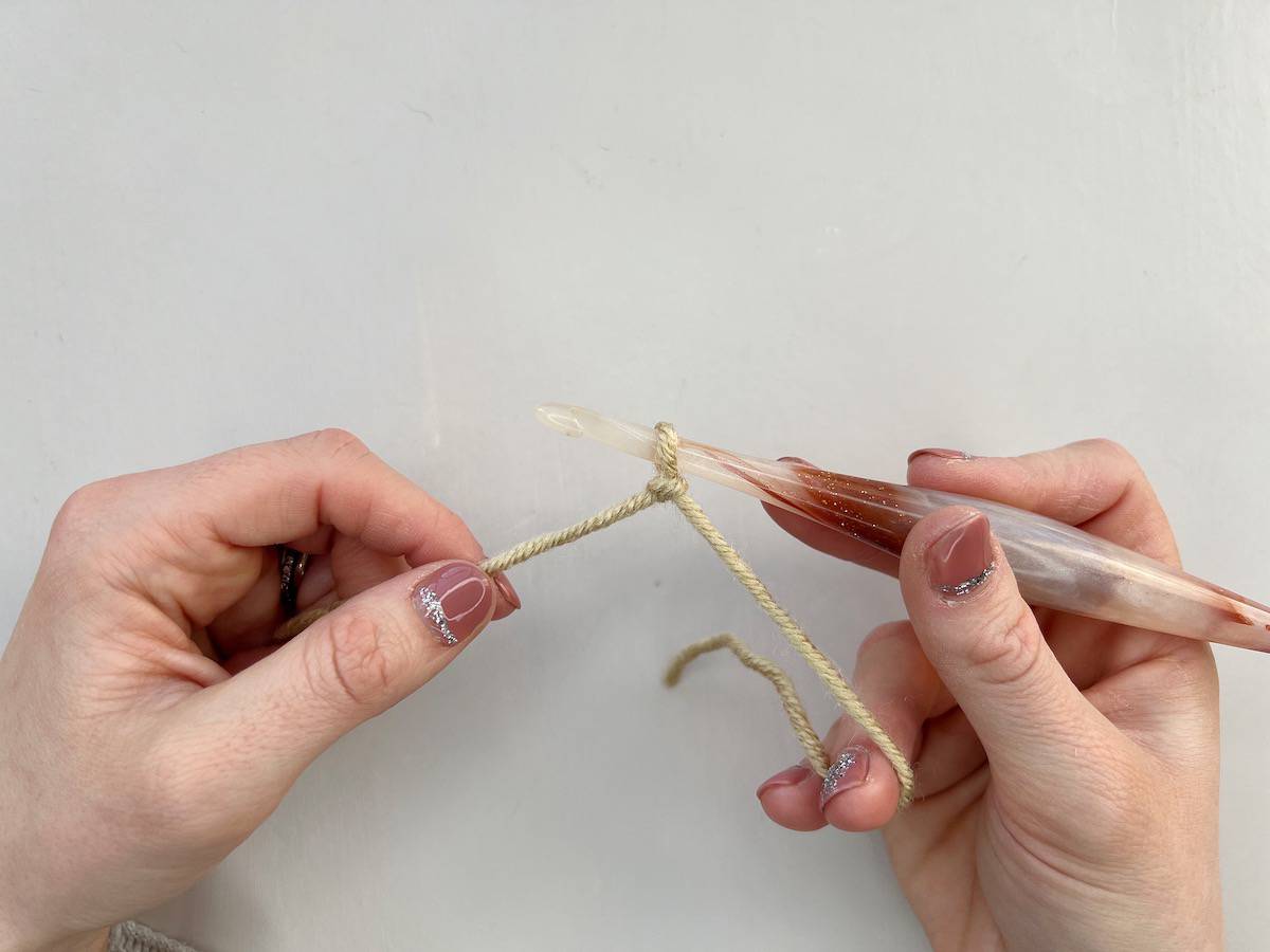 A person's hands showing step 1 of creating a crochet chain stitch, which is to create a slipknot on your hook.
