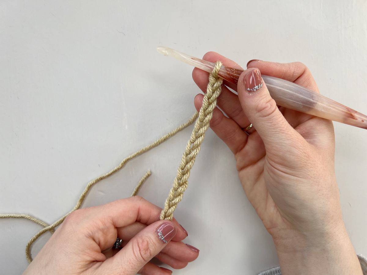 A person using a crochet hook to make a series of chain stitches to complete a foundation chain.