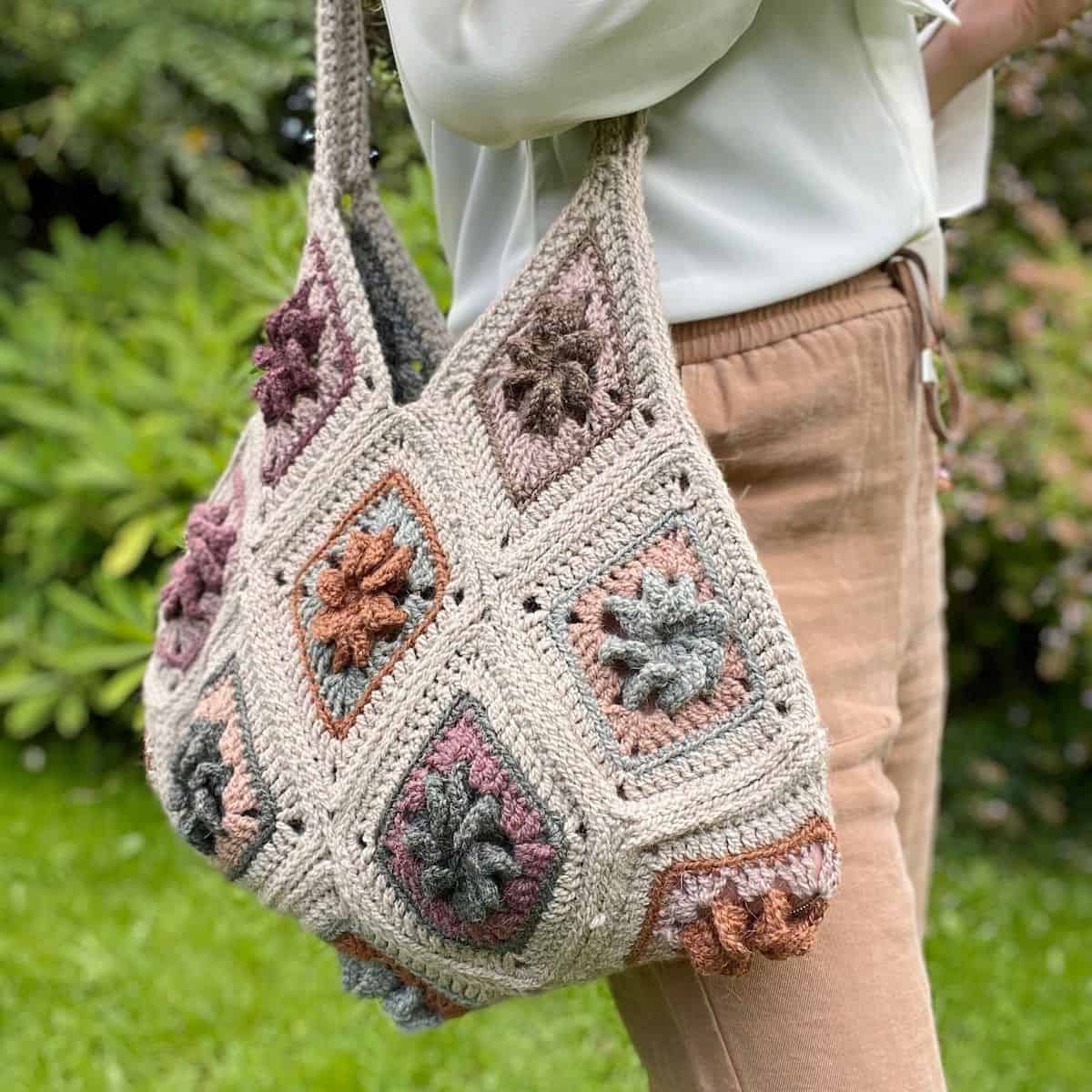 A woman is holding a crocheted bag in the grass.