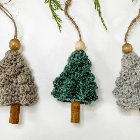 Three knitted christmas trees hanging on a branch.