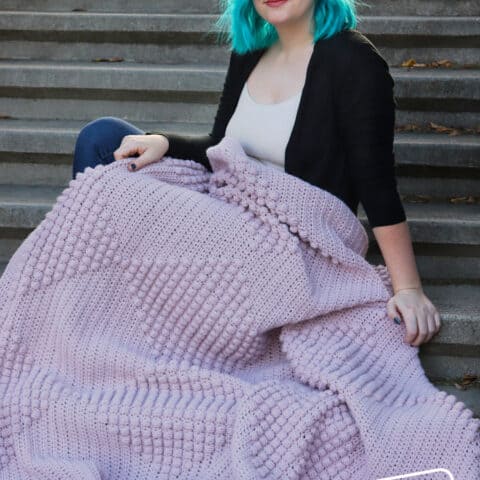A woman with blue hair sitting on steps with a purple blanket.