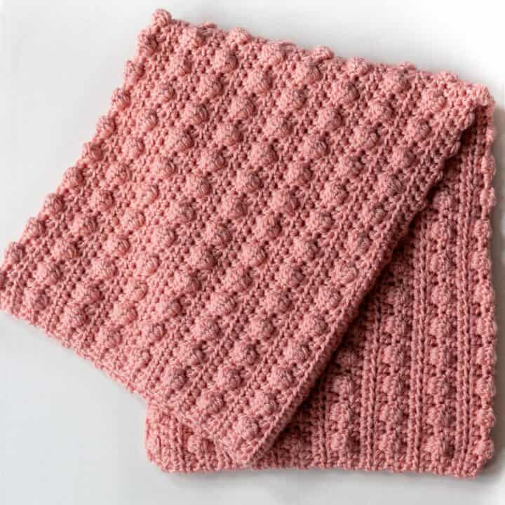 A pink crocheted blanket on a white surface.