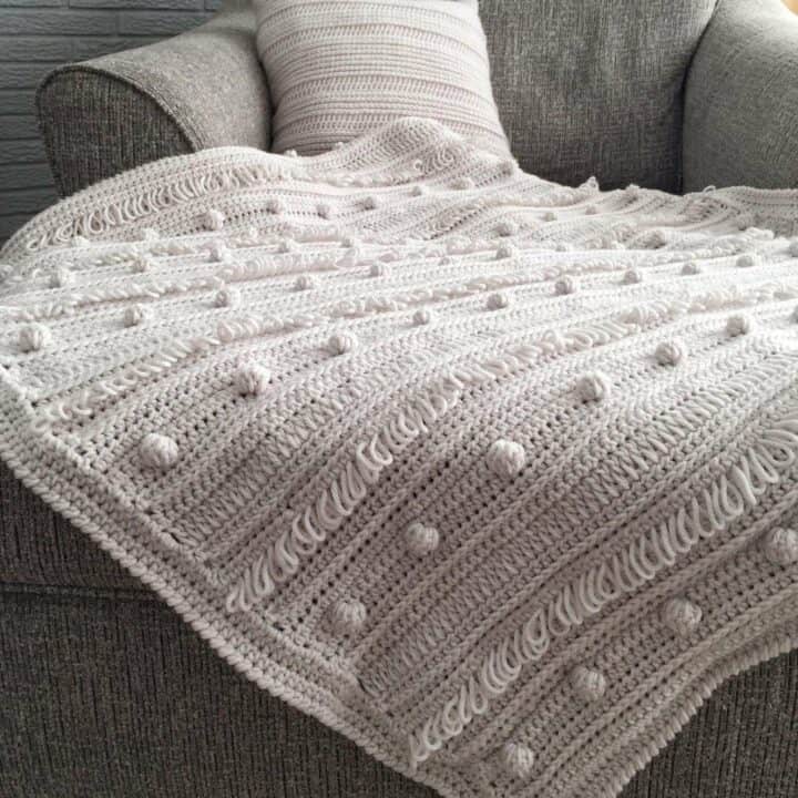 A white crocheted blanket sitting on a couch.