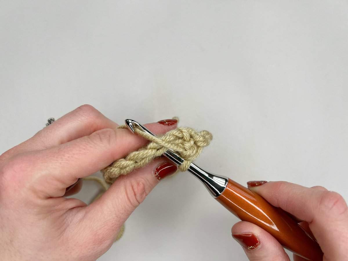 A person using a crochet hook to make a split extended single crochet stitch - step 2 yarn over hook and pull through a loop.
