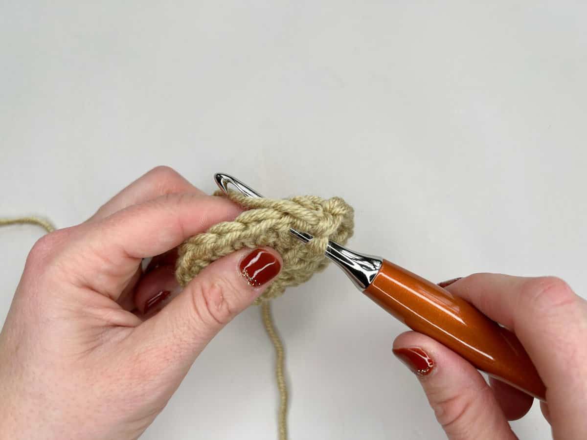 A person is using a crochet hook to make a waistcoat crochet stitch: step 2 - yarn over and pull through a loop.