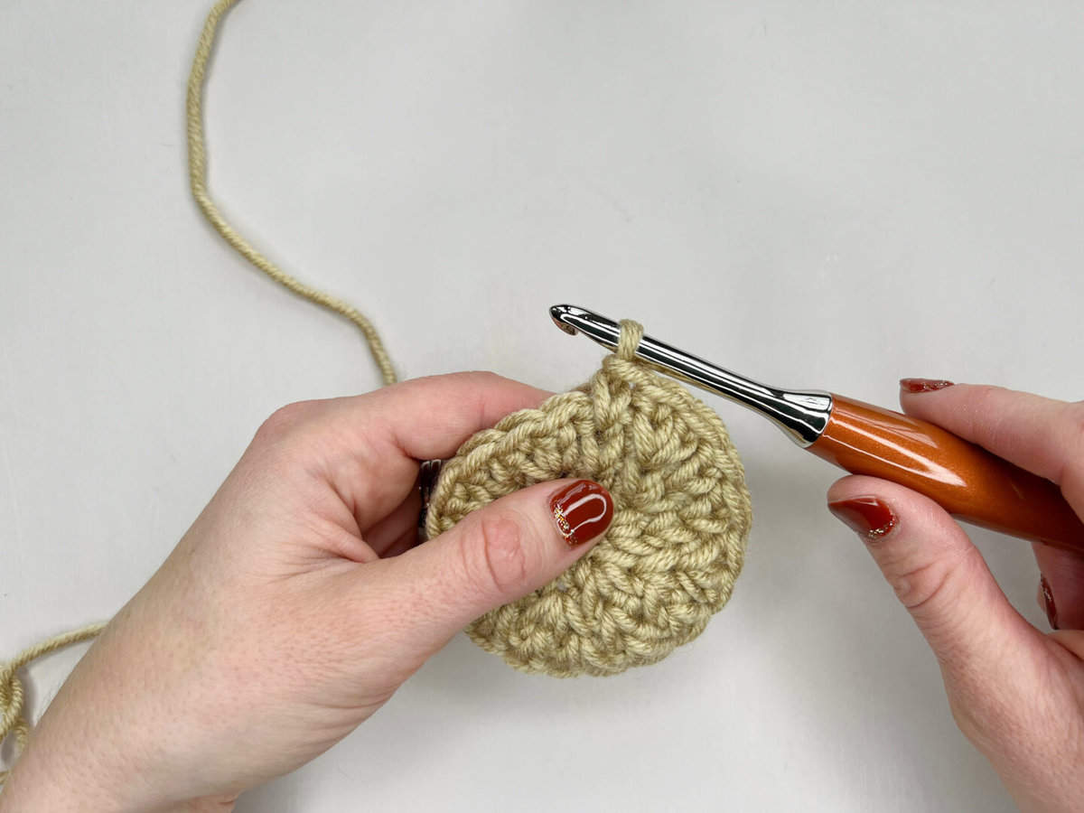 A person using the waistcoat crochet stitch to make a crocheted circle - a completed waistcoat stitch is shown.