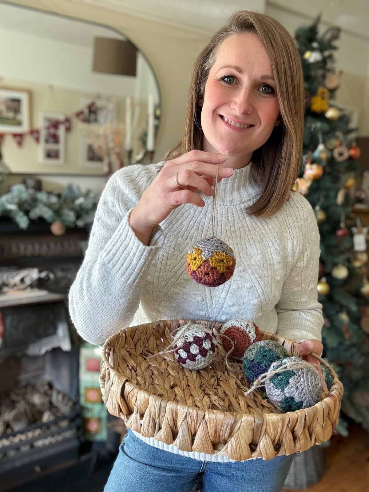 A woman holding a basket of crocheted ornaments in front of a christmas tree.