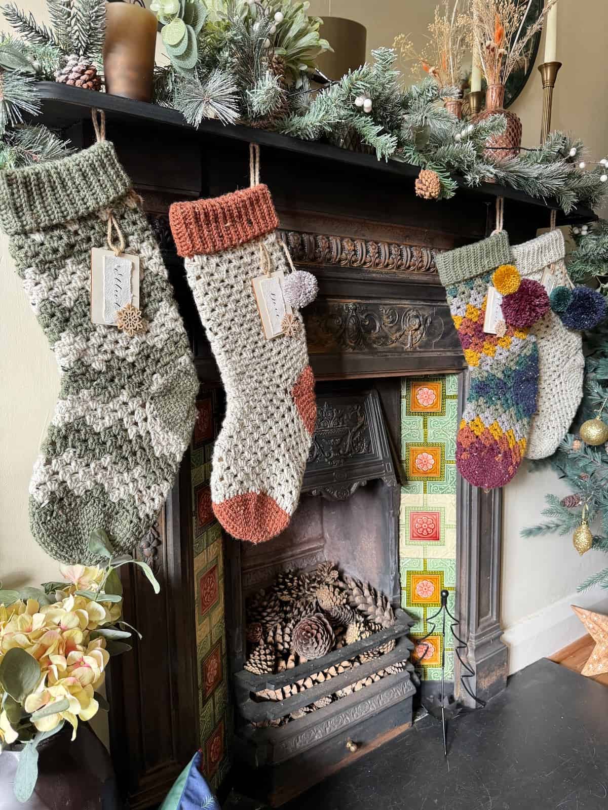 Three crocheted Christmas stockings hanging on a fireplace in rustic colours.