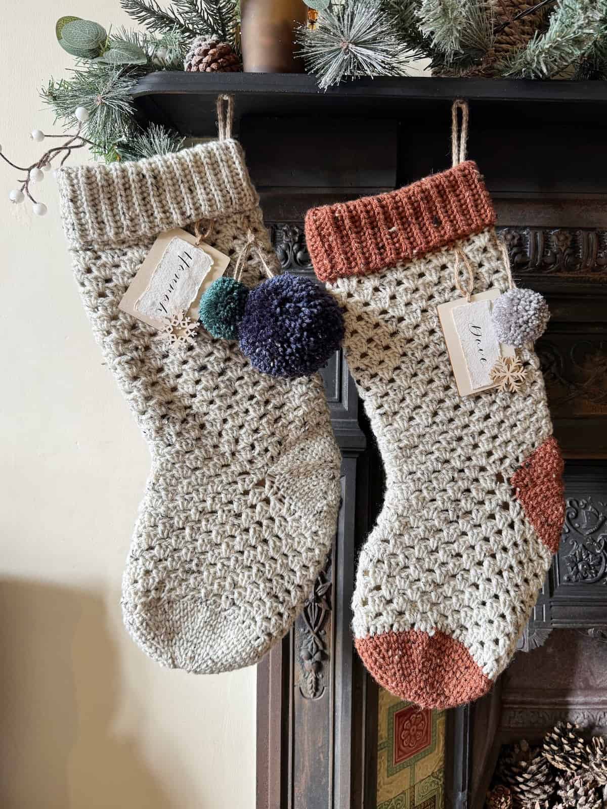 Two crochet christmas stockings using the granny stitch hanging on a fireplace.