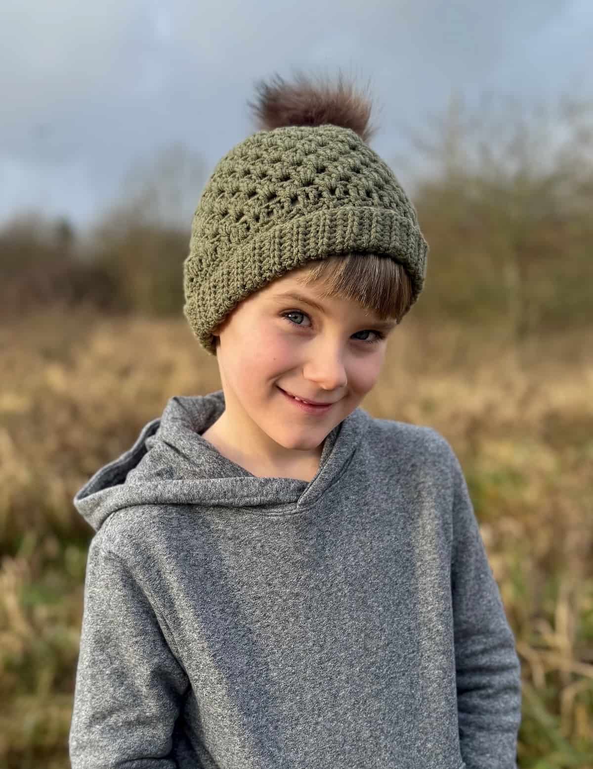 A young boy wearing a green crocheted hat with a pom pom.