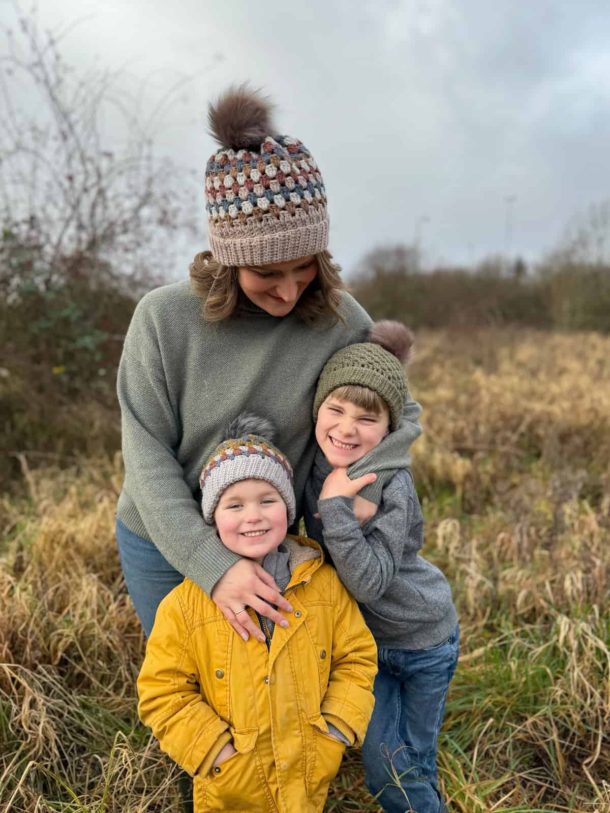 A woman and two children standing in a field wearing hats.