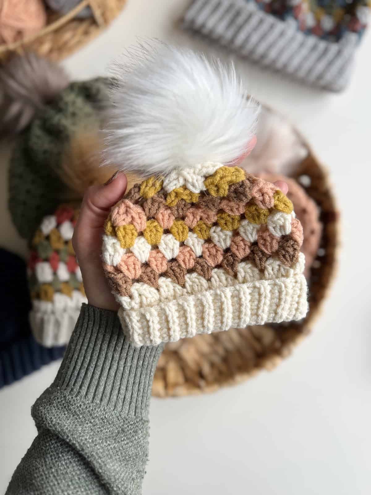 A person holding a crocheted hat with a pom pom.