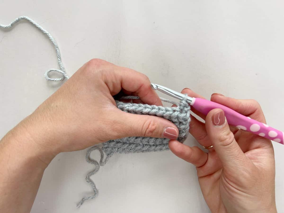 A person is using a pink crochet hook to show a completed yarn over slip stitch.