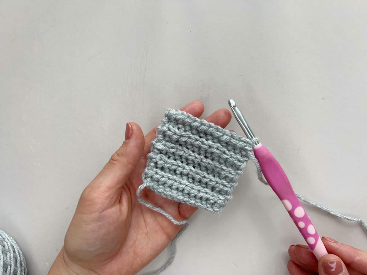 A person holding a crocheted yarn over slip stitch sample with a pink crochet hook.