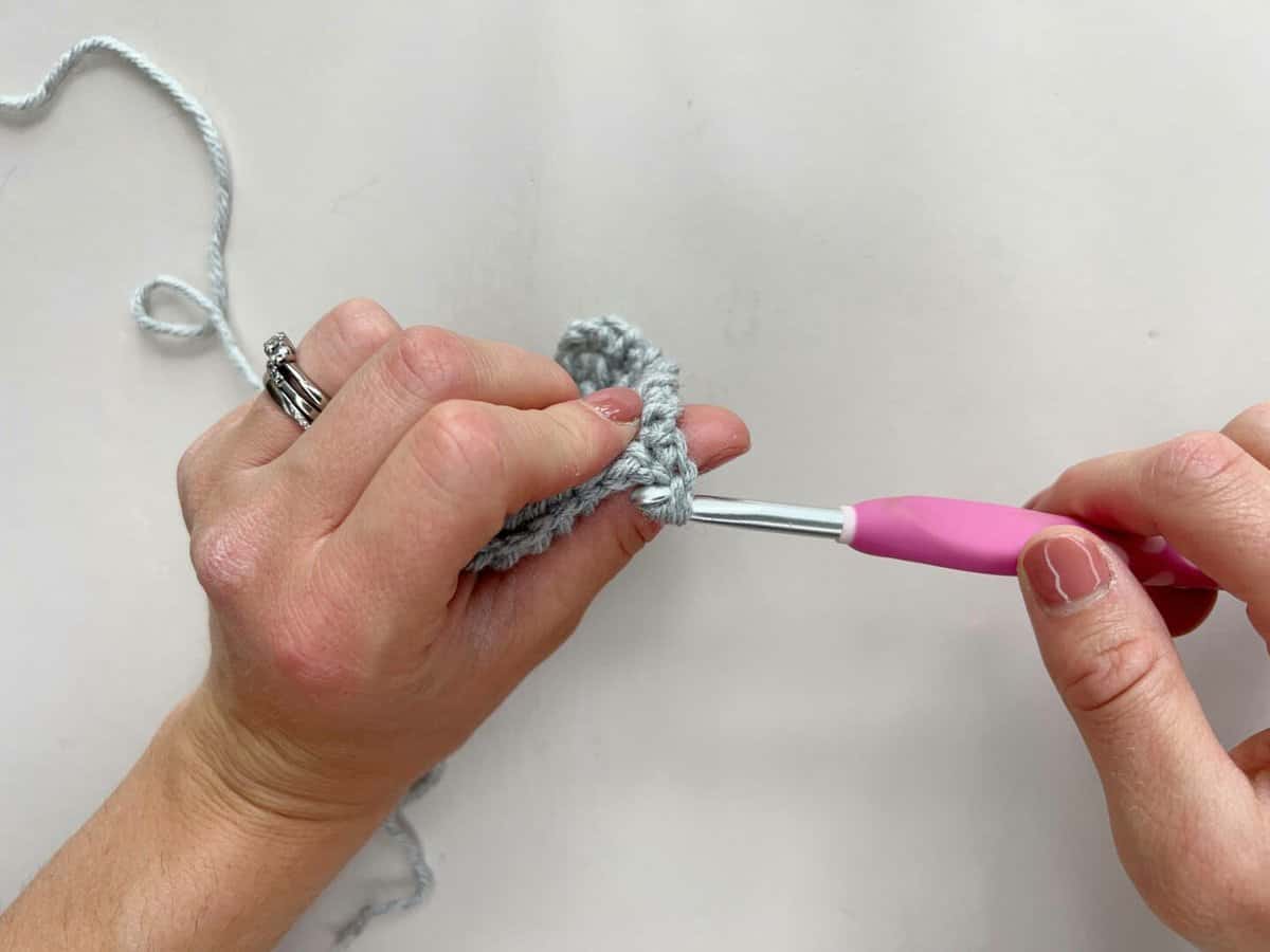 A person is using a pink crochet hook to make a yarn over slip stitch.