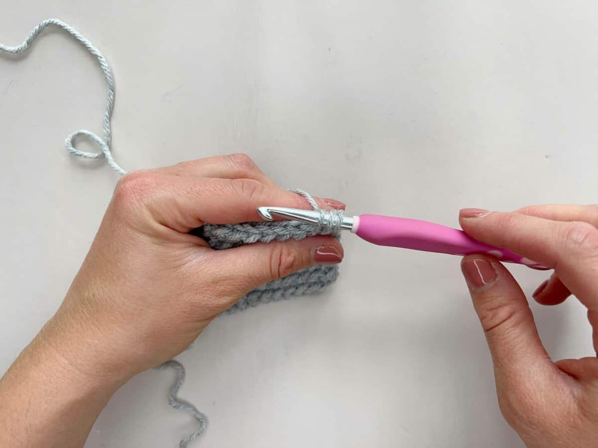 A person using a pink crochet hook to make a yarn over slip stitch.