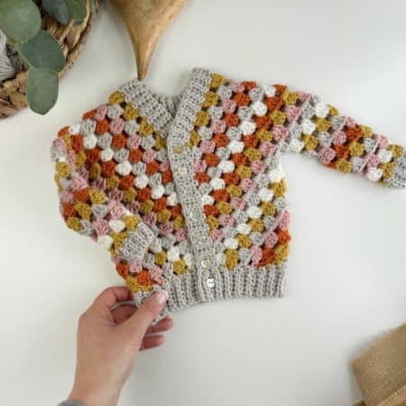 A hand holding a crocheted cardigan.