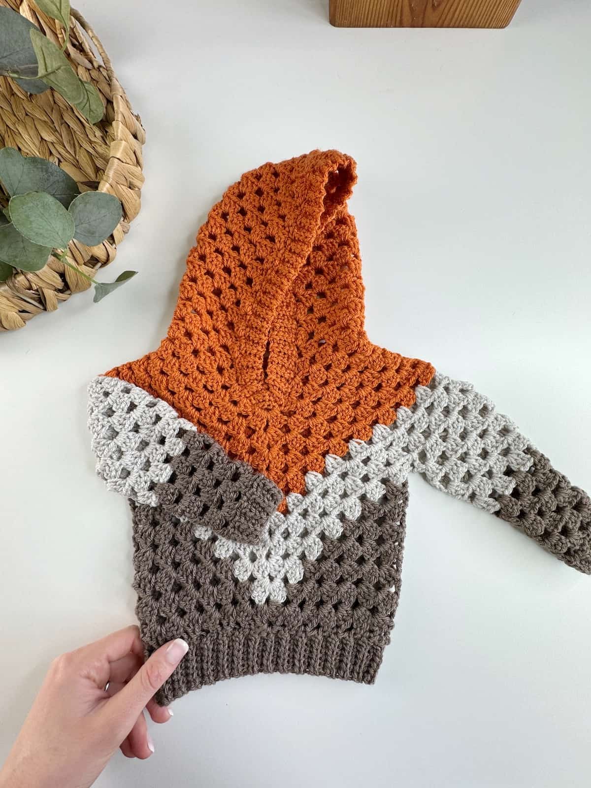 A hand holding a crocheted orange and grey hoodie.