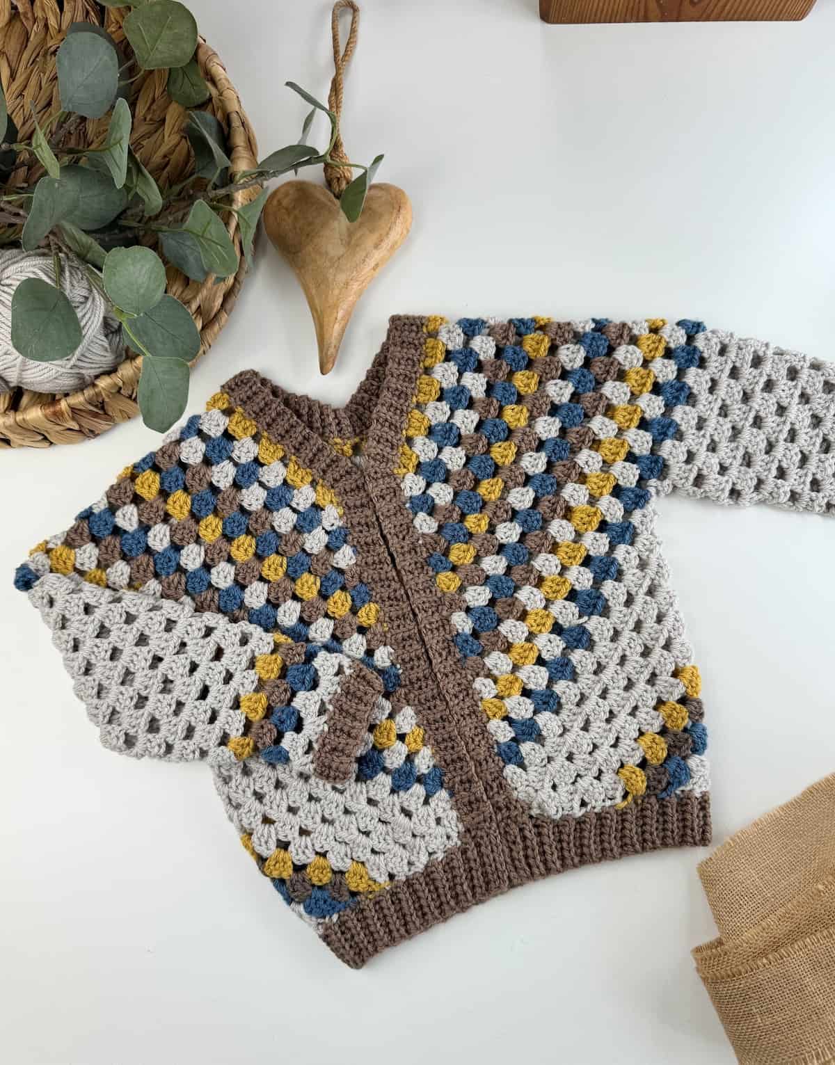 A granny stripe crochet cardigan for boys on a table next to a basket.