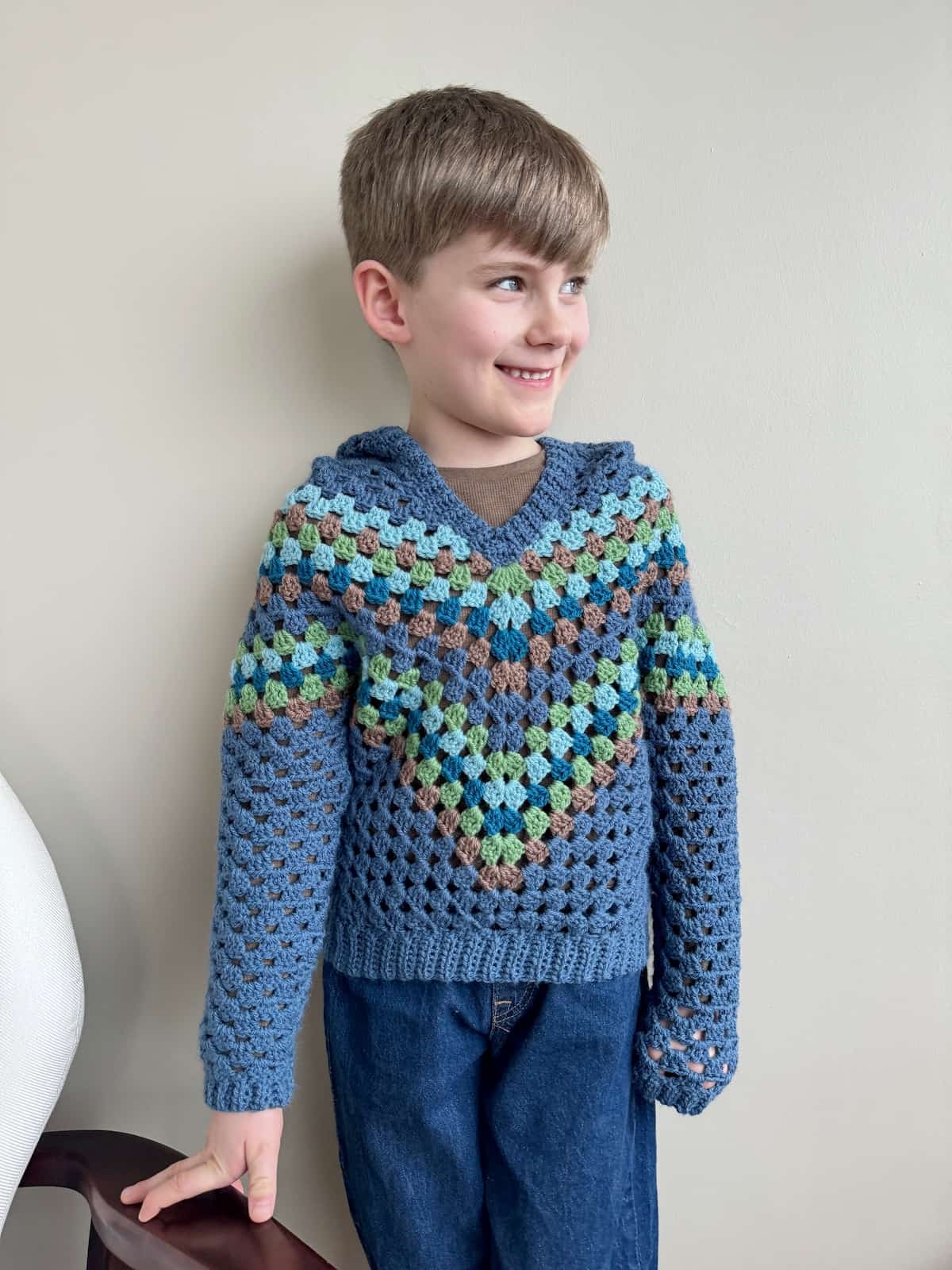 A young boy wearing a blue crocheted hoodie and jeans.