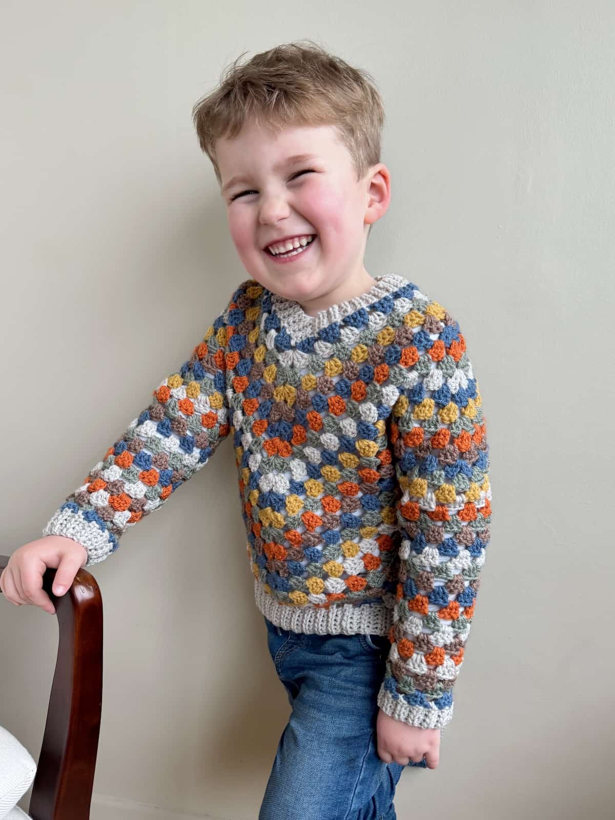 A child wearing a granny stitch sweater sits on a chair.