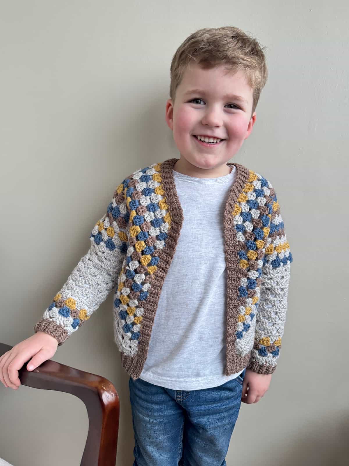 A young boy wearing a crochet cardigan in granny stitch.