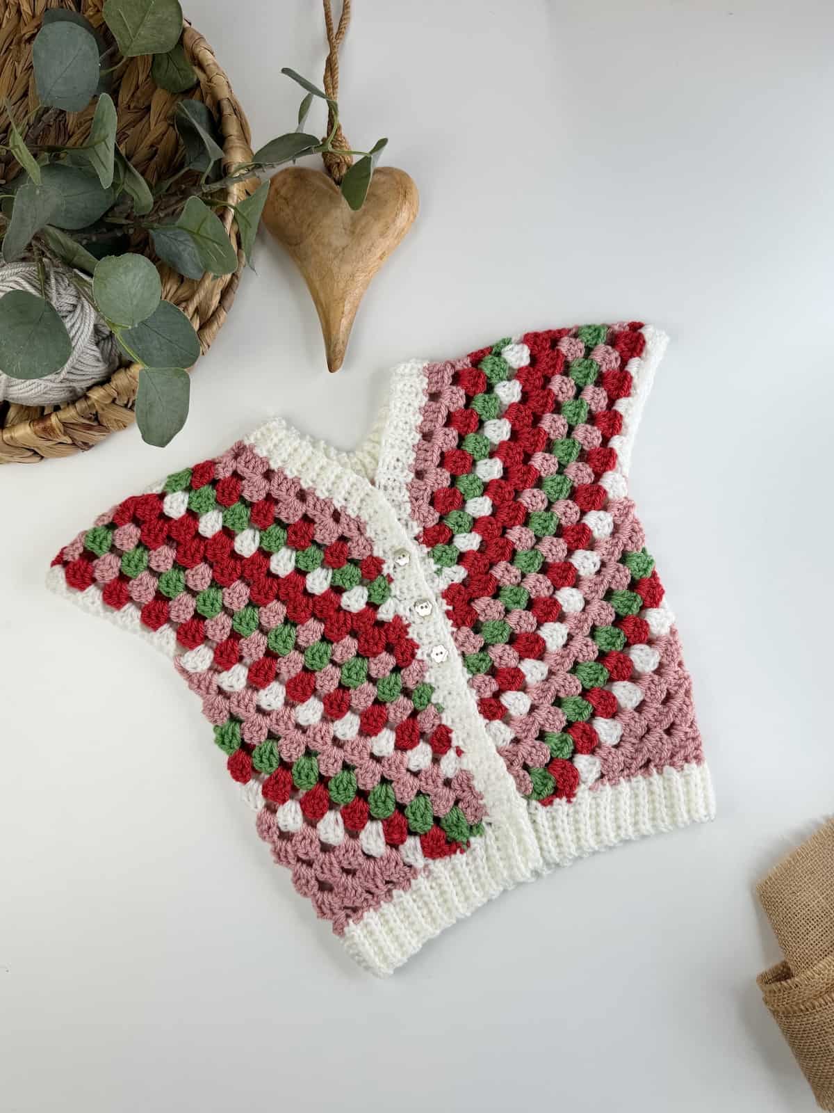 A sleeveless crocheted cardigan for toddlers with red, green and white stripes.