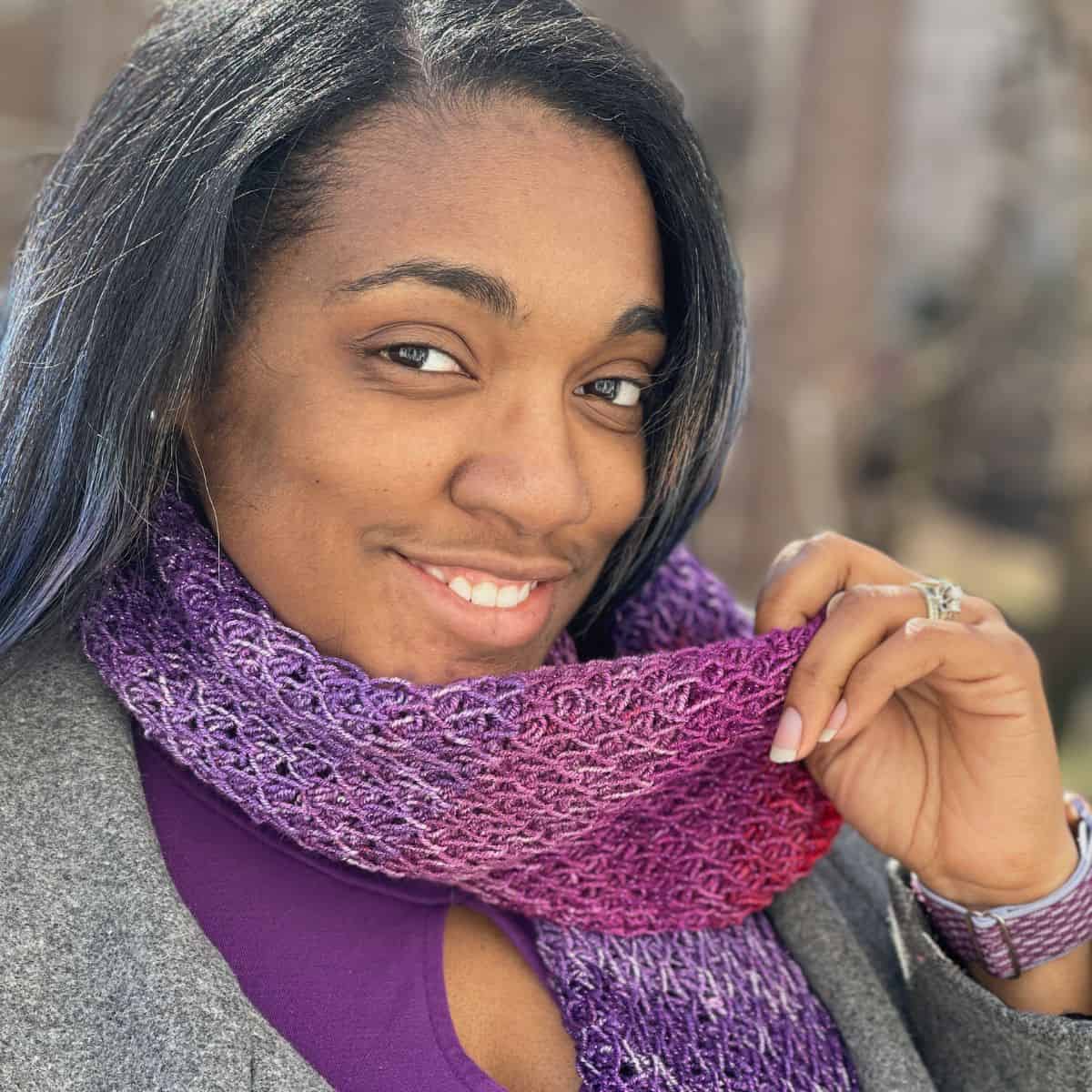 A woman wearing a crochet purple and pink scarf.