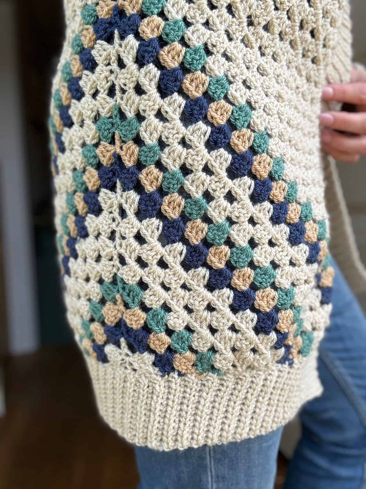 Close-up of a person holding the side of a crochet cardigan in the granny stitch with stripes.