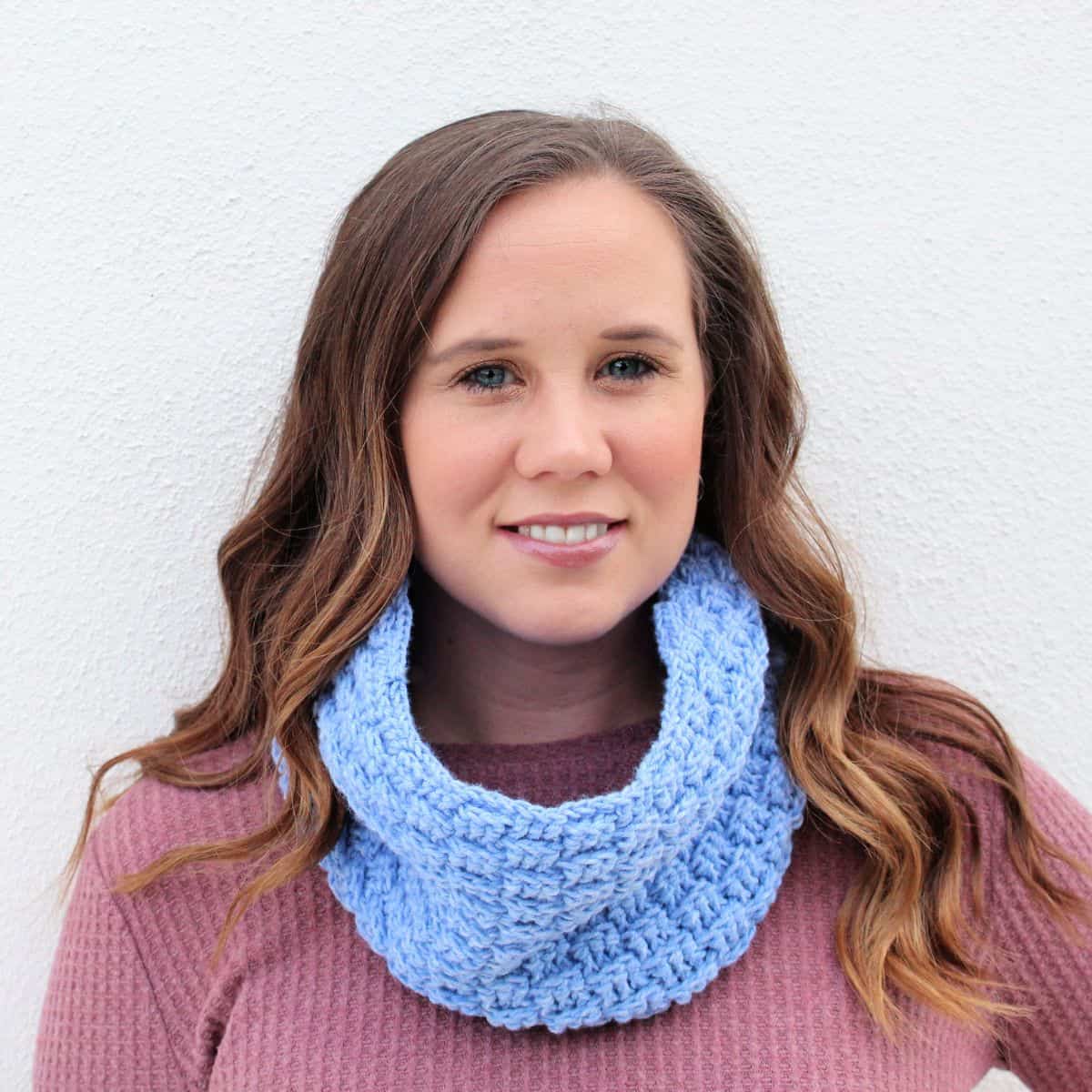 A woman wearing a blue crochet cowl scarf.