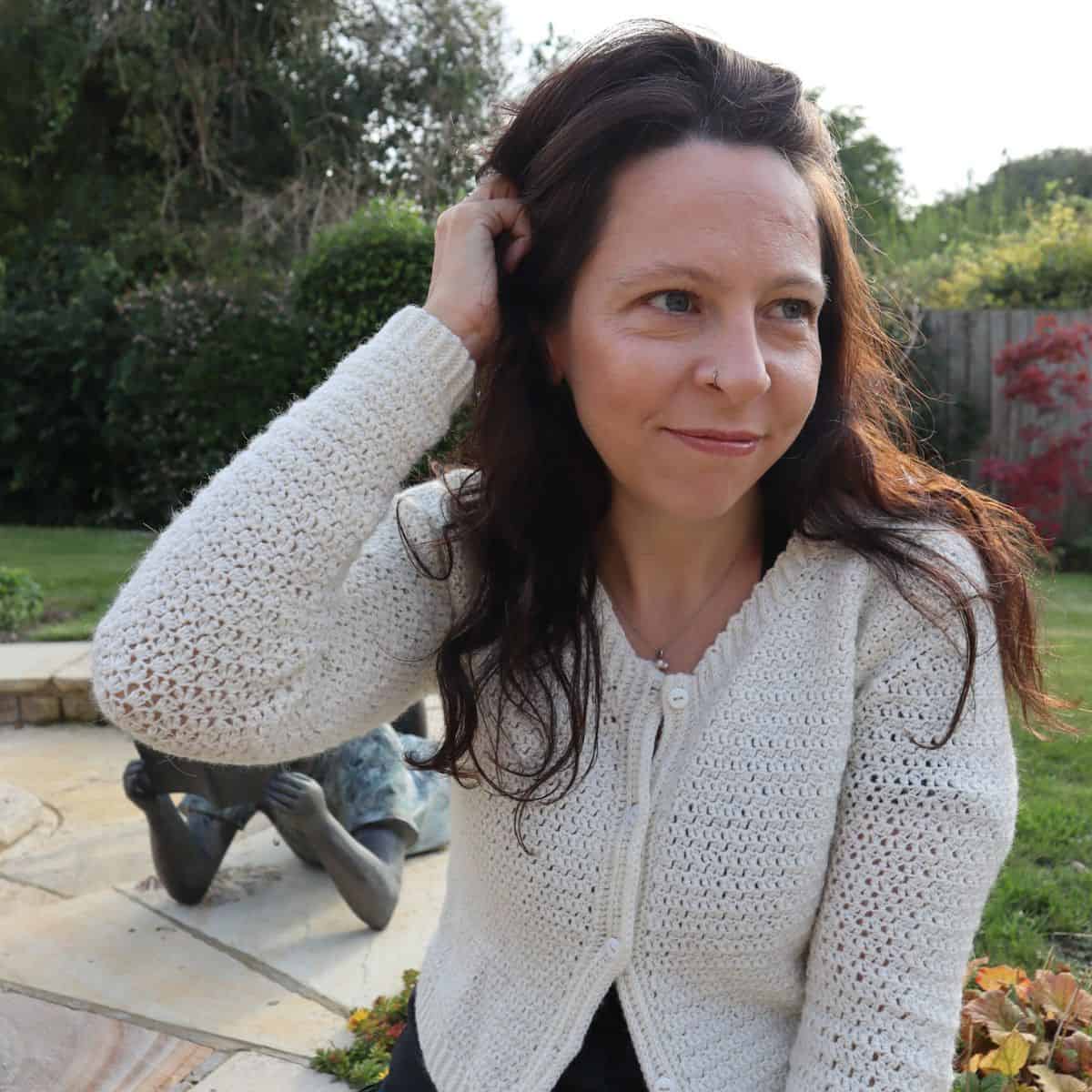 A woman wearing a white crochet cardigan in a garden.