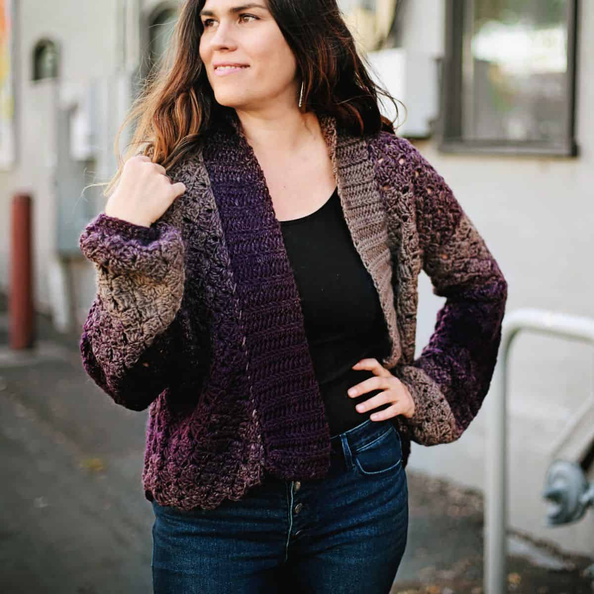 A woman wearing a purple crochet cardigan and jeans.