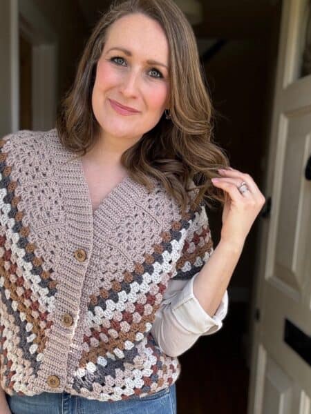 A woman standing in a doorway wearing a crocheted vest over a white shirt.