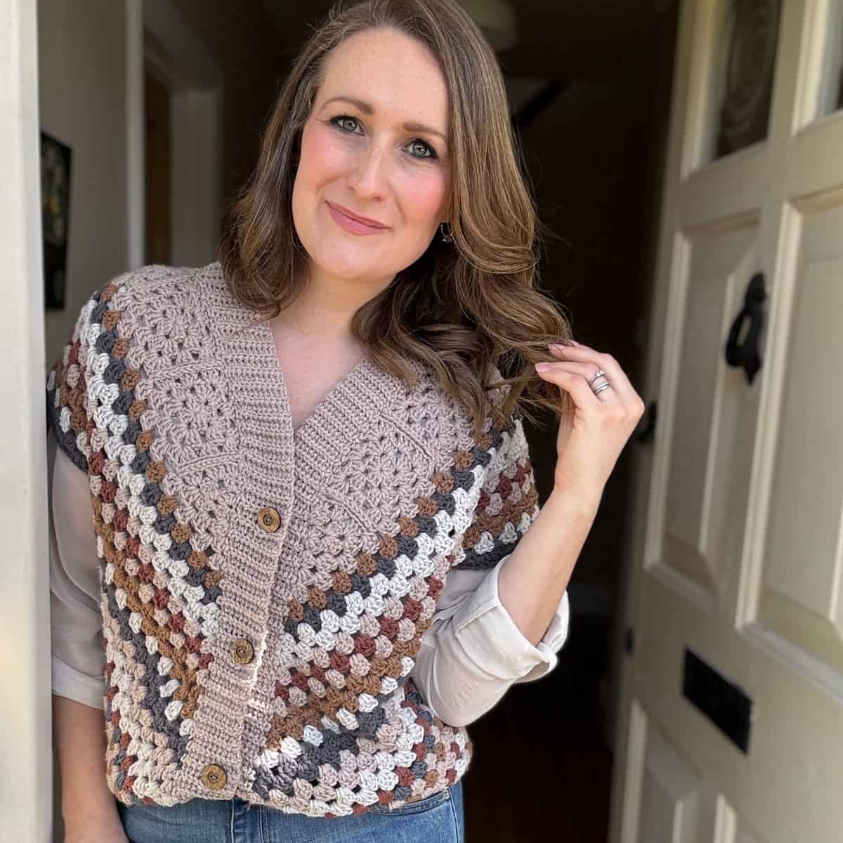 A woman standing in a doorway wearing a crocheted vest over a white shirt.