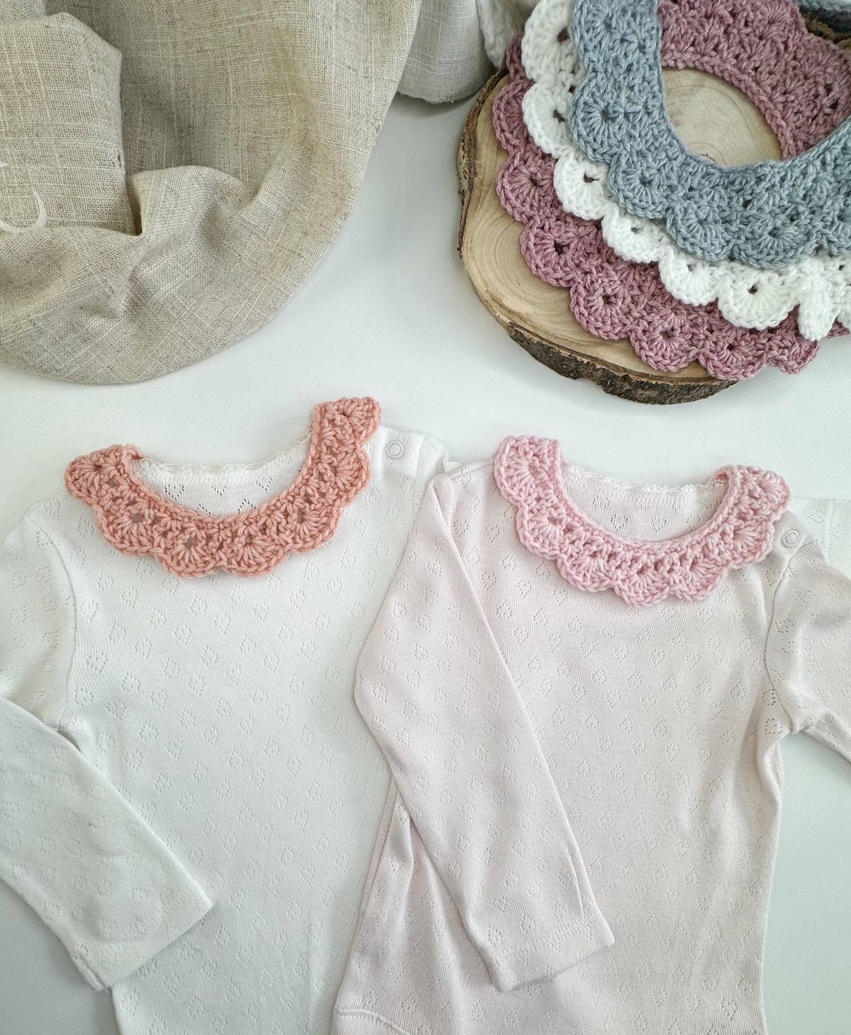 Baby size crocheted collars added to a babygrow on a wooden table.