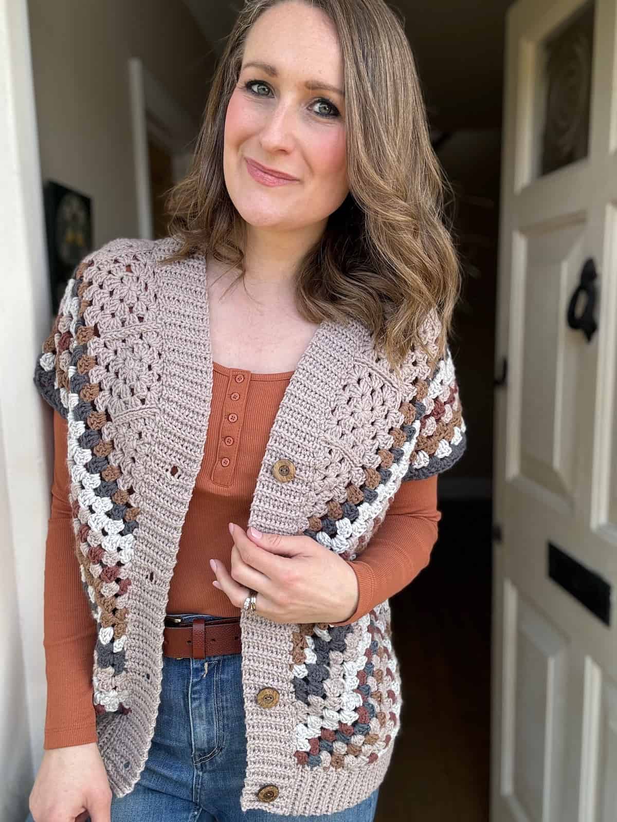 Woman smiling in a handmade granny square crochet cardigan standing indoors.