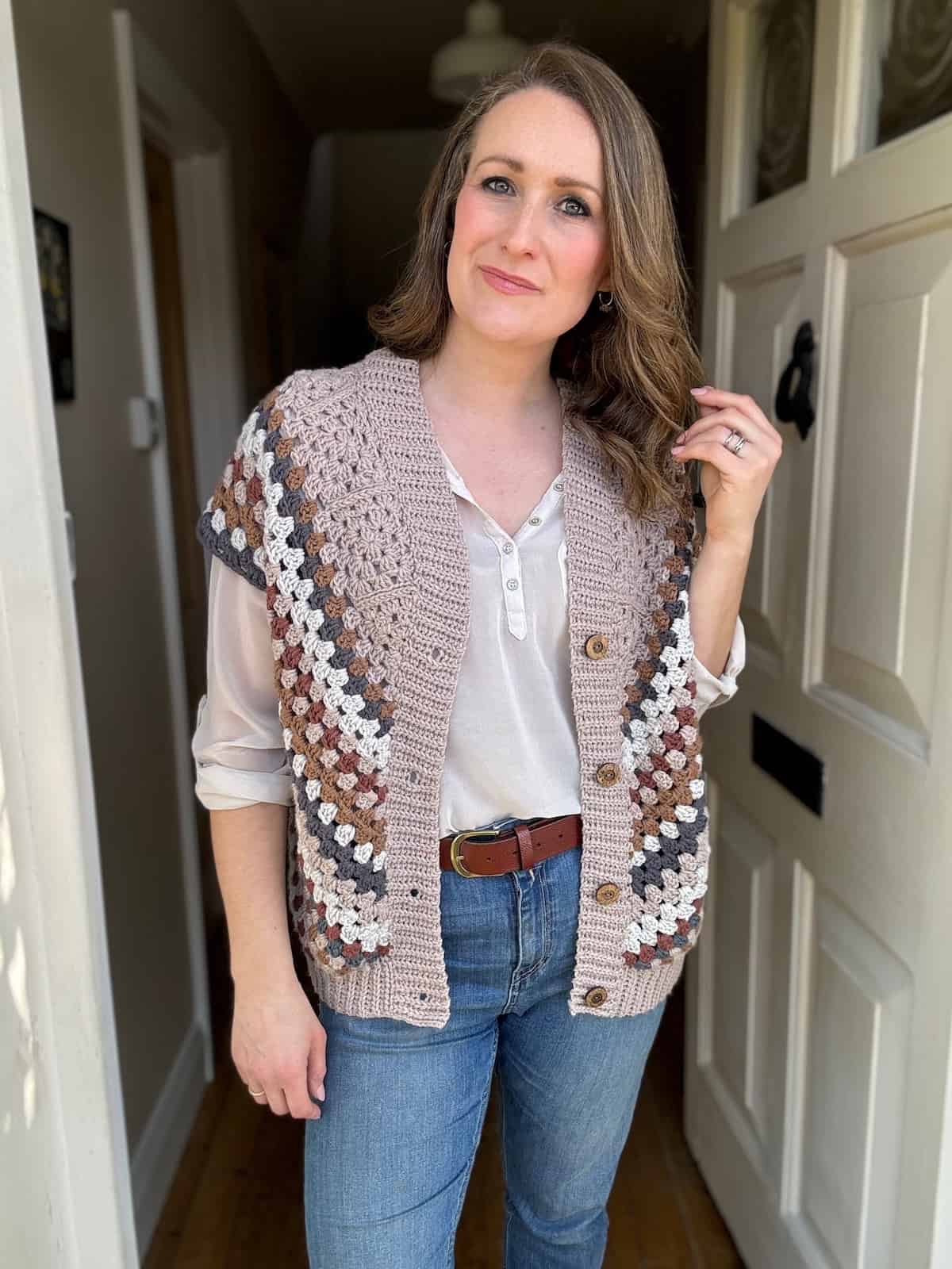 Woman in a crocheted vest and jeans standing indoors.