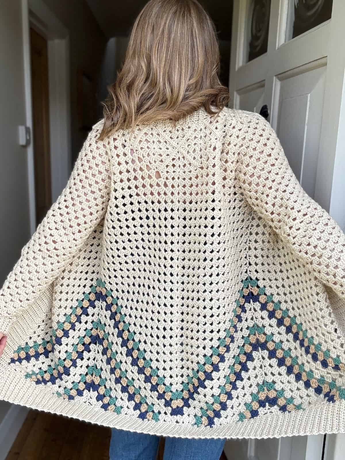 Person showcasing the back of a handmade crochet cardigan with a granny squares design.