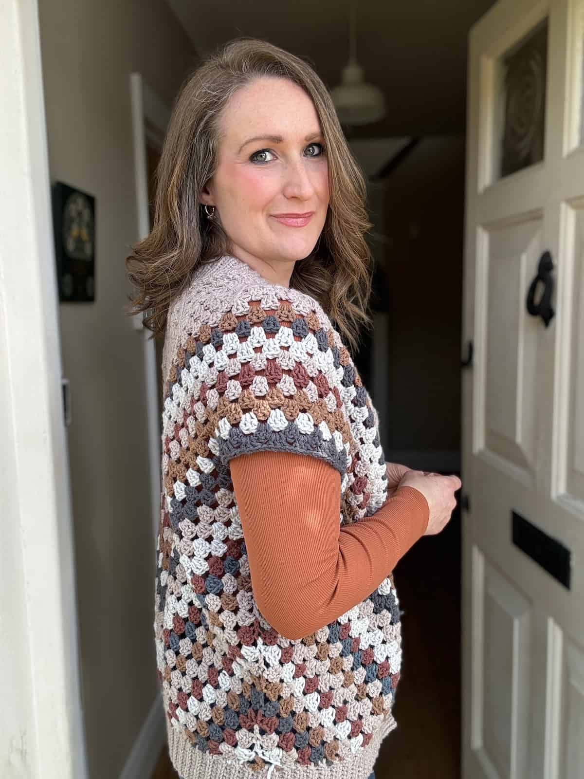 A woman in a striped crochet cardigan standing by an open door, glancing over her shoulder.