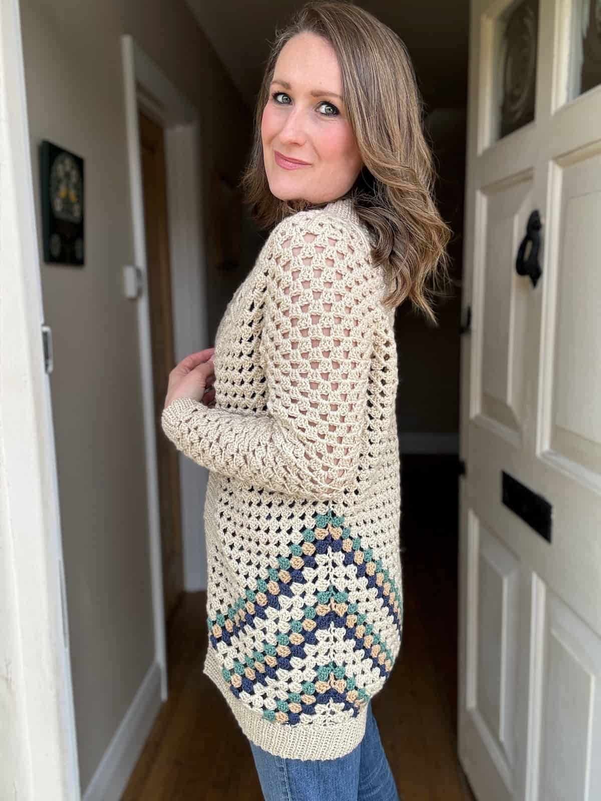 Woman posing in a hallway wearing a beige crochet cardigan.