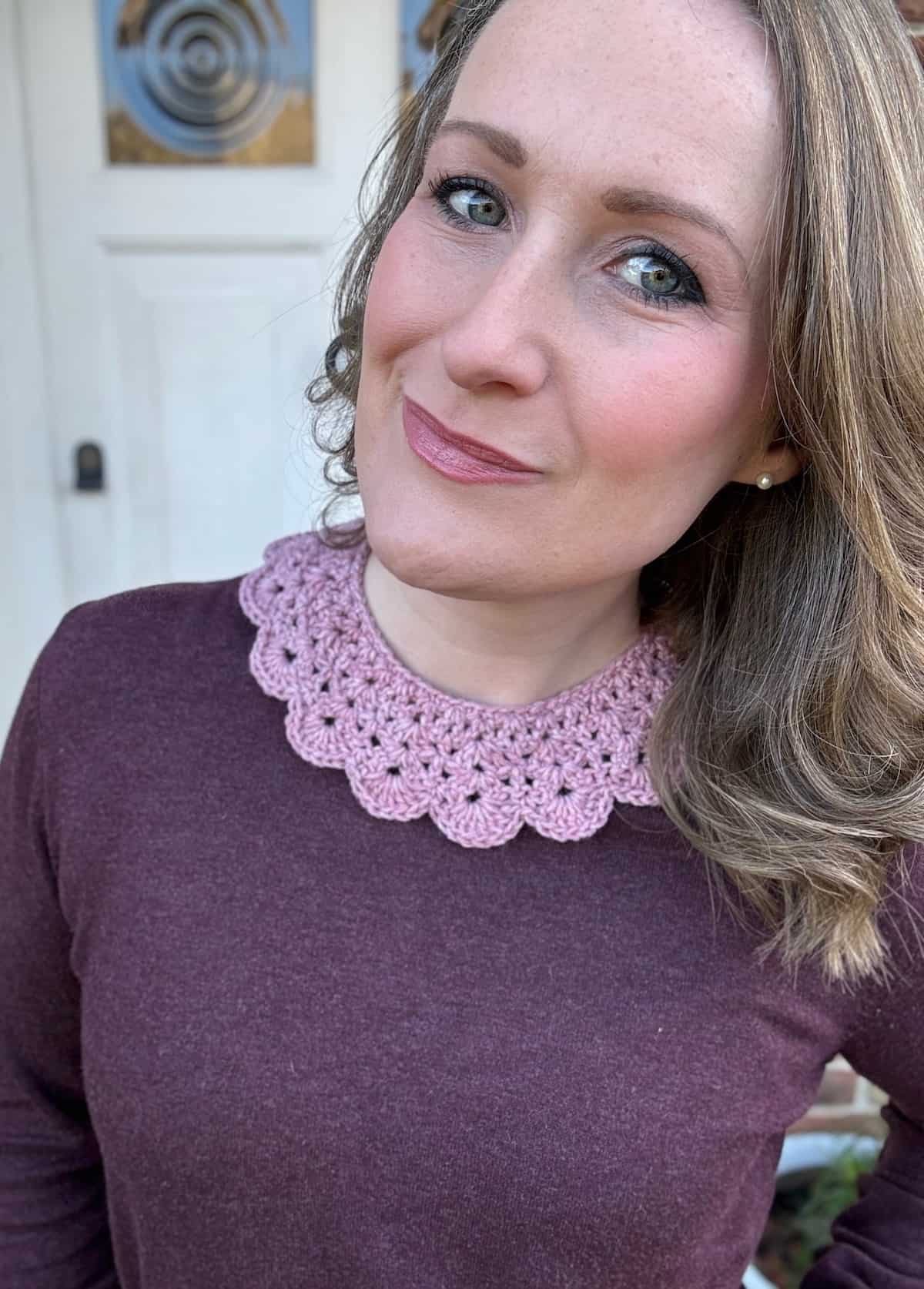 A woman wearing a burgundy sweater and pink crocheted collar.