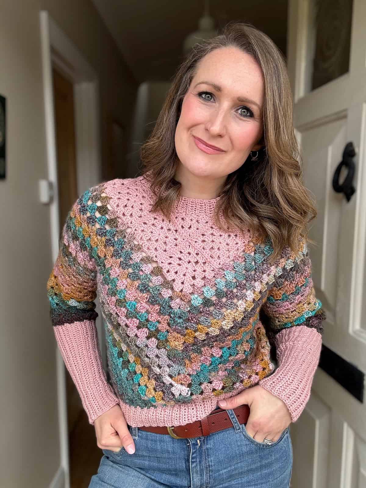 Woman in doorway wearing colourful granny square sweater.